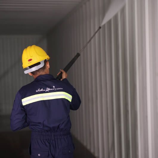 A shipping container being washed by a high-pressure cleaning system